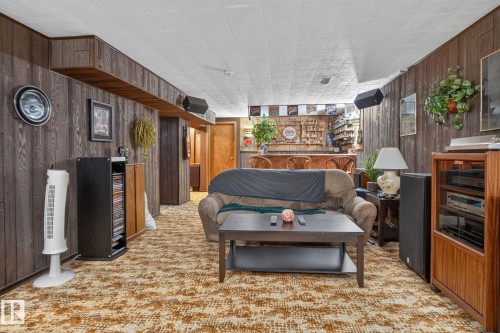 Recreation room featuring wood paneling, wall-to-wall carpeting, and a built-in bar with a wooden countertop and bar stools - 4712 131 Avenue Nw, Edmonton, AB 