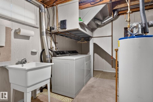 Dedicated laundry area featuring a utility sink with a chrome faucet, washer and dryer appliances, and a water heater - 4712 131 Avenue Nw, Edmonton, AB 