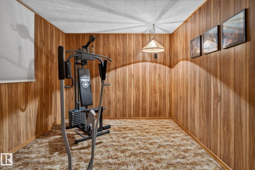 Spacious room featuring wood paneling, patterned carpet flooring, and a drop ceiling with a central pendant light fixture - 4712 131 Avenue Nw, Edmonton, AB 