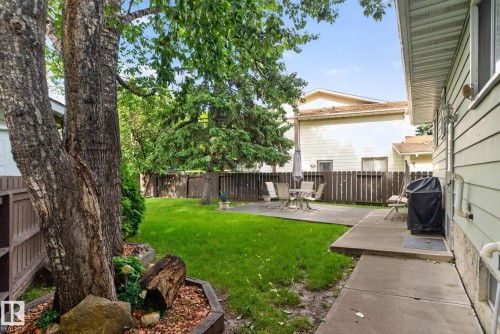 Spacious backyard featuring a manicured lawn, established shade trees, a concrete patio, a privacy fence, and light-colored exterior siding - 4712 131 Avenue Nw, Edmonton, AB 