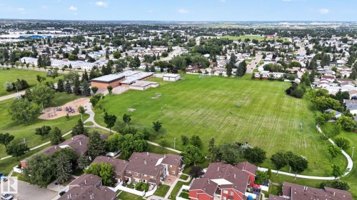 Expansive green space featuring a large sports field, adjacent playground, paved walking paths, and mature trees - 4712 131 Avenue Nw, Edmonton, AB 