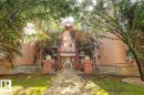 Brick multi-story building featuring a central entrance with stairs, white railings, and mature trees - 107 10153 117 Street, Edmonton, AB 