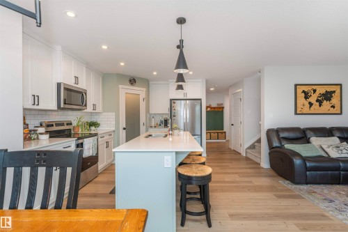 Modern kitchen featuring white cabinetry, stainless steel appliances, a subway tile backsplash, and a light-toned island with pendant lighting - 102 Horton Way, Ardrossan, AB 