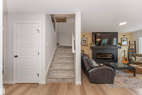 Bright living area featuring wood-finish flooring and a modern fireplace with a black surround - 102 Horton Way, Ardrossan, AB 