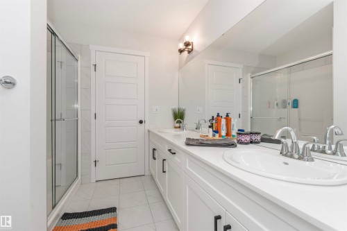 Bathroom featuring a dual vanity with white countertops, chrome faucets, and white cabinetry with black hardware - 102 Horton Way, Ardrossan, AB 