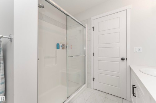 Contemporary shower enclosure featuring a sliding glass door, white surround, and integrated shelving - 102 Horton Way, Ardrossan, AB 