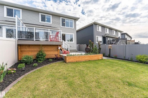 Expansive backyard featuring a manicured lawn, a raised wooden deck with glass panel railings, and a lower patio area - 102 Horton Way, Ardrossan, AB 