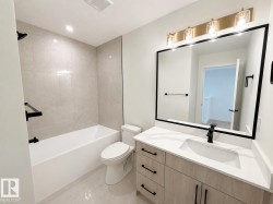 Bathroom featuring a light wood-finish vanity with a quartz countertop, an integrated rectangular sink, and a matte black faucet - 