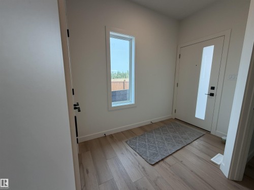 Entryway featuring a white door with vertical glass insert, black hardware, wood-finish flooring, and a tall vertical window - 115 Pierwyck Loop, Spruce Grove, AB 