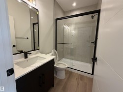 Bathroom featuring a black-framed glass shower enclosure, a dark wood-finish vanity with a white countertop and integrated sink, a matte black faucet, and wood-finish flooring - 
