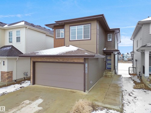 Modern two-story residence with a multi-toned facade, featuring a large attached garage, a blue entry door, and prominent windows on the upper level - 19066 20A Avenue, Edmonton, AB 