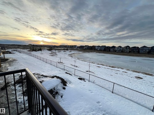 Black metal railing overlooking an expansive snow-covered landscape with a frozen pond and distant residential structures - 19066 20A Avenue, Edmonton, AB 