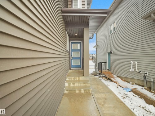Entryway featuring a contemporary blue door with frosted glass panels, sheltered by an extended soffit with recessed lighting - 19066 20A Avenue, Edmonton, AB 