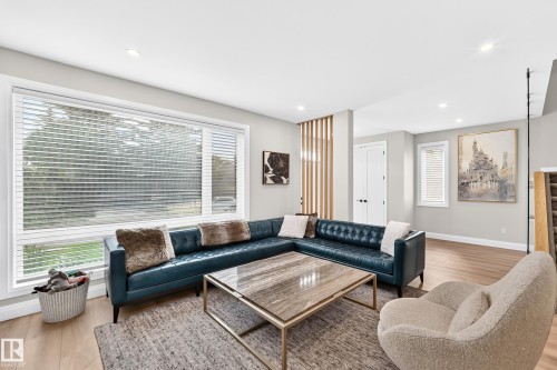 Spacious living area featuring large windows with blinds, recessed lighting, wood-finish flooring, a decorative wood slat partition, and painted walls - 12631 52 Avenue, Edmonton, AB 