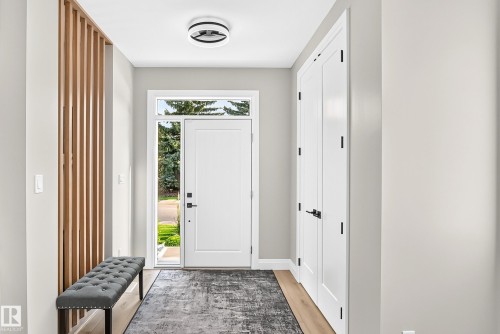 Foyer featuring a contemporary wood slat accent wall, a white entry door with frosted sidelight and transom, and wood-finish flooring - 12631 52 Avenue, Edmonton, AB 