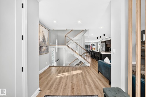 Bright interior featuring wood-finish flooring, a modern staircase with clear panel railings and wood handrails, recessed lighting, and white baseboards - 12631 52 Avenue, Edmonton, AB 