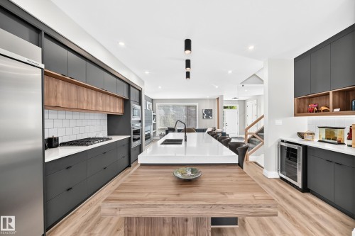 Gourmet kitchen with dark flat-panel cabinetry, wood-finish flooring, integrated stainless steel appliances, and a central island featuring a white countertop with an undermount sink - 12631 52 Avenue, Edmonton, AB 