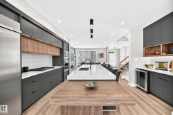 Gourmet kitchen with dark flat-panel cabinetry, wood-finish flooring, integrated stainless steel appliances, and a central island featuring a white countertop with an undermount sink - 