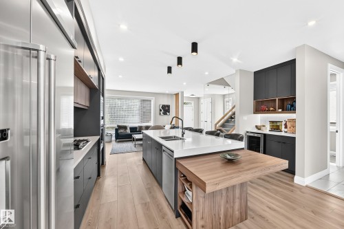 Open-concept kitchen with wood-finish flooring, stainless steel refrigerator, white countertops, a large island with integrated wood-finish dining extension, and built-in bar area with beverage cooler - 12631 52 Avenue, Edmonton, AB 