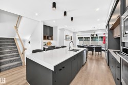 Open-concept space featuring light wood-finish flooring, a long kitchen island with a light-toned countertop, and dark cabinetry - 