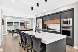 Modern kitchen featuring a large white countertop island with integrated seating, dark flat-panel cabinetry, stainless steel appliances, and wood-finish flooring - 