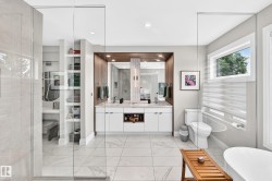 Spacious bathroom featuring large format tile flooring, a dual vanity with a wood-finish surround, a built-in shelving system, a window with horizontal blinds, and a freestanding soaking tub - 
