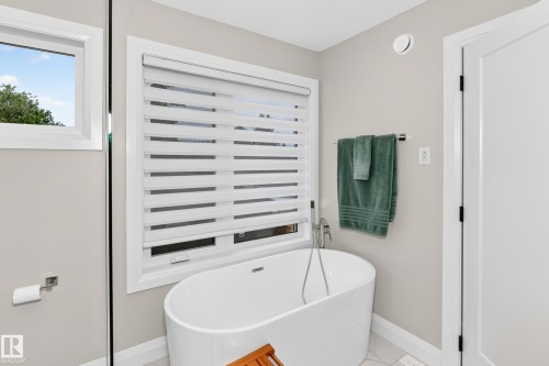 Freestanding soaking tub with floor-mounted faucet, accented by a large window with privacy blinds - 12631 52 Avenue, Edmonton, AB 
