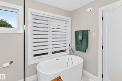 Freestanding soaking tub with floor-mounted faucet, accented by a large window with privacy blinds - 
