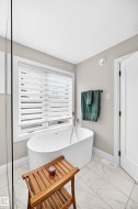 Freestanding soaking tub with floor-mounted faucet, set against a window with layered privacy blinds - 