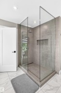 Modern walk-in shower featuring clear glass panels, a rainfall showerhead, and a recessed niche - 