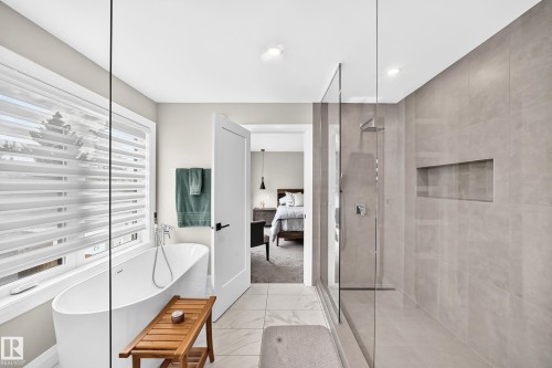 Contemporary bathroom featuring a freestanding soaking tub with floor-mounted fixtures, a spacious glass-enclosed shower with a built-in niche, light-toned large format tile flooring, and integrated ceiling lighting - 12631 52 Avenue, Edmonton, AB 