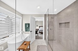 Contemporary bathroom featuring a freestanding soaking tub with floor-mounted fixtures, a spacious glass-enclosed shower with a built-in niche, light-toned large format tile flooring, and integrated ceiling lighting - 