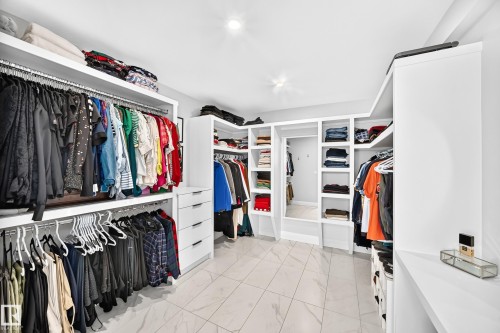 Spacious walk-in closet featuring extensive built-in shelving, multiple hanging rods, integrated drawers with modern pulls, and light-toned tile flooring - 12631 52 Avenue, Edmonton, AB 