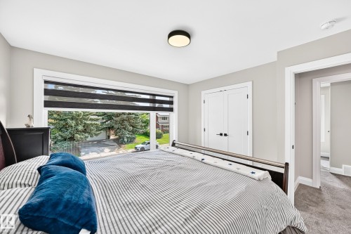 Bedroom featuring a large window with privacy blinds, dual white panel doors, wall-to-wall carpeting, and a flush-mount ceiling light - 12631 52 Avenue, Edmonton, AB 