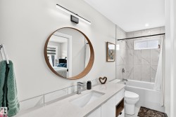 Bathroom featuring a contemporary floating vanity with an integrated sink, a large circular mirror with a wood-finish frame, and a sleek linear light fixture - 