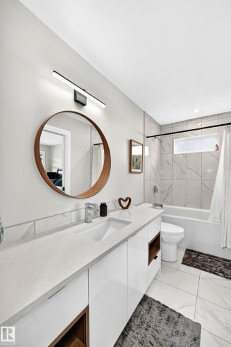 Contemporary bathroom featuring a white vanity with an integrated sink, a large round mirror, and a sleek linear light fixture - 12631 52 Avenue, Edmonton, AB 
