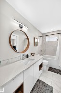 Contemporary bathroom featuring a white vanity with an integrated sink, a large round mirror, and a sleek linear light fixture - 