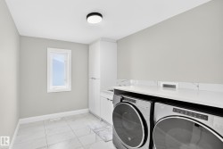 Dedicated laundry room featuring light gray walls, a single window with white trim, and white tile flooring - 
