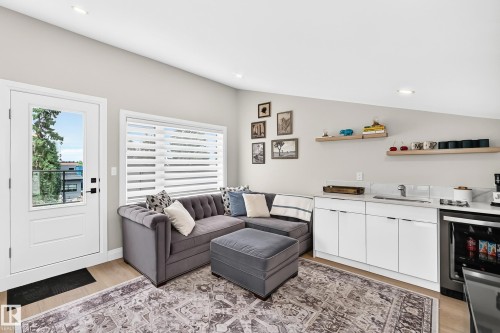 Open-concept living area featuring light wood-finish flooring, recessed lighting, a built-in wet bar with white cabinetry, a stainless steel sink, and a beverage refrigerator - 12631 52 Avenue, Edmonton, AB 