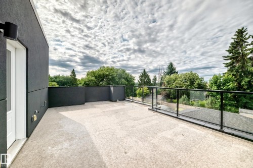Spacious rooftop patio featuring light-toned concrete flooring, dark stucco exterior, a white entry door, and a glass panel railing system with black posts - 12631 52 Avenue, Edmonton, AB 
