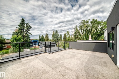 Rooftop deck featuring a glass railing system, textured concrete surface, and a contemporary dark gray exterior wall with an exterior light fixture - 12631 52 Avenue, Edmonton, AB 