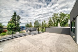 Rooftop deck featuring a glass railing system, textured concrete surface, and a contemporary dark gray exterior wall with an exterior light fixture - 