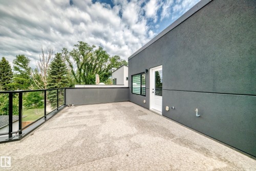 Spacious rooftop deck featuring a glass railing, dark gray stucco exterior, white entry door, and horizontal window blinds - 12631 52 Avenue, Edmonton, AB 