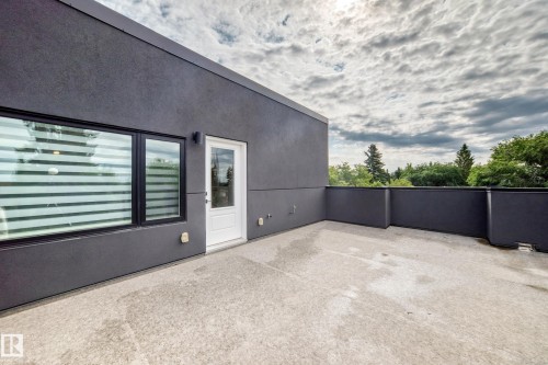 Expansive rooftop deck featuring a concrete surface, dark grey exterior walls, a white exterior door, and black-framed windows - 12631 52 Avenue, Edmonton, AB 