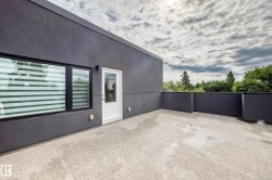 Expansive rooftop deck featuring a concrete surface, dark grey exterior walls, a white exterior door, and black-framed windows - 