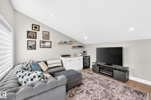 Vaulted ceiling living area featuring wood-finish flooring, a built-in wet bar with white cabinetry, under-counter beverage refrigerator, and recessed lighting - 12631 52 Avenue, Edmonton, AB 