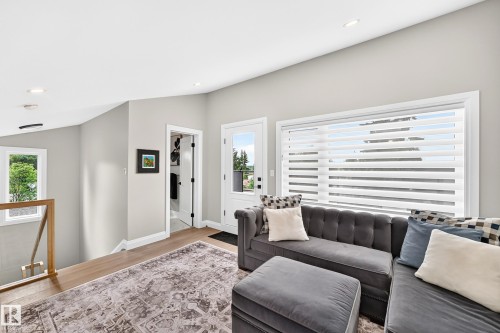 Upper-level living area featuring wood-finish flooring, recessed lighting, expansive window with horizontal blinds, and a glass-paneled door opening to an exterior space - 12631 52 Avenue, Edmonton, AB 