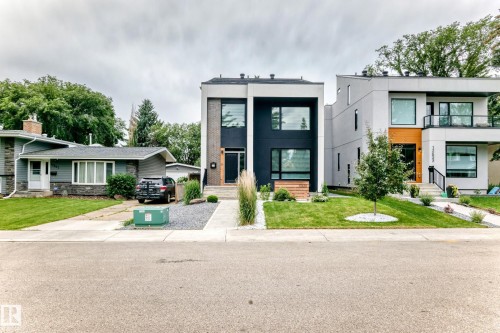Modern facade with striking black and white paneling, large rectangular windows, a prominent wood-finish entry door, a gravel and concrete pathway, and a manicured front lawn - 12631 52 Avenue, Edmonton, AB 