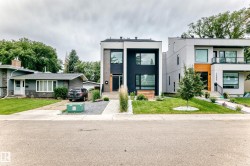 Modern facade with striking black and white paneling, large rectangular windows, a prominent wood-finish entry door, a gravel and concrete pathway, and a manicured front lawn - 