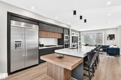 Gourmet kitchen featuring a large waterfall island with integrated sink, stainless steel appliances, modern cabinetry with wood accents, and a subway tile backsplash - 12631 52 Avenue, Edmonton, AB 